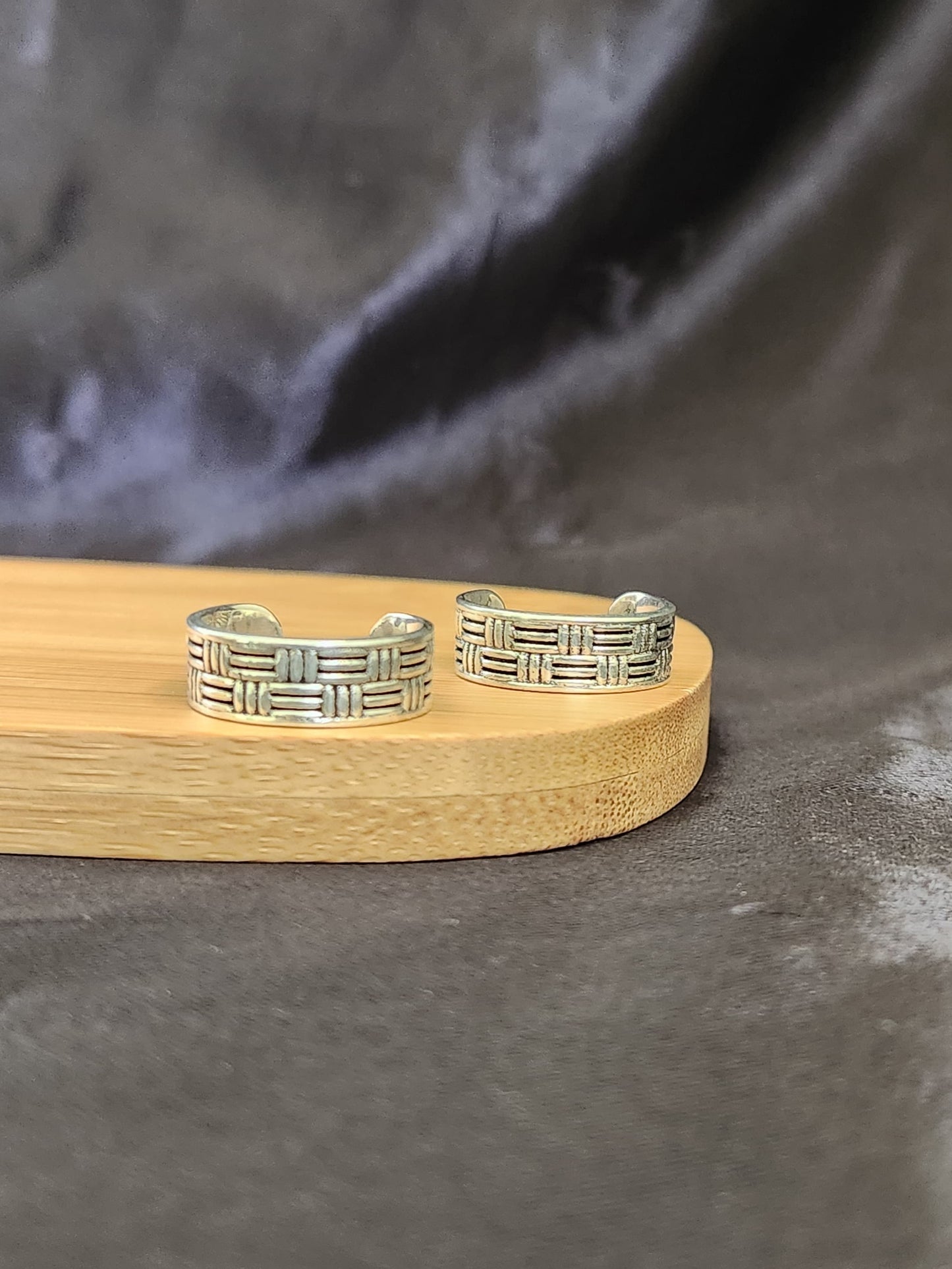 A pair of elegant silver toe rings with a polished finish, featuring delicate designs and an adjustable open band.