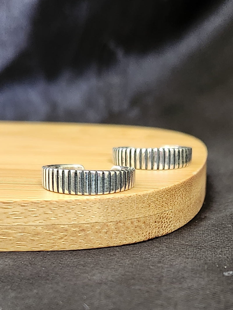 A pair of elegant silver toe rings with a polished finish, featuring delicate designs and an adjustable open band.