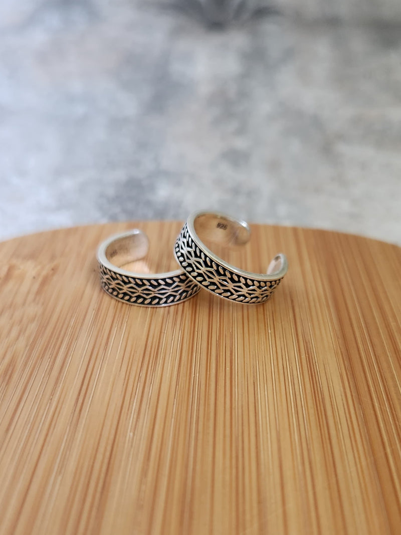 A pair of elegant silver toe rings with a polished finish, featuring delicate designs and an adjustable open band.