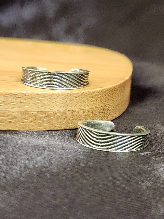 A pair of elegant silver toe rings with a polished finish, featuring delicate designs and an adjustable open band.
