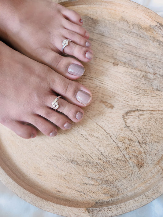 A pair of elegant silver toe rings with a polished finish, featuring delicate designs and an adjustable open band.