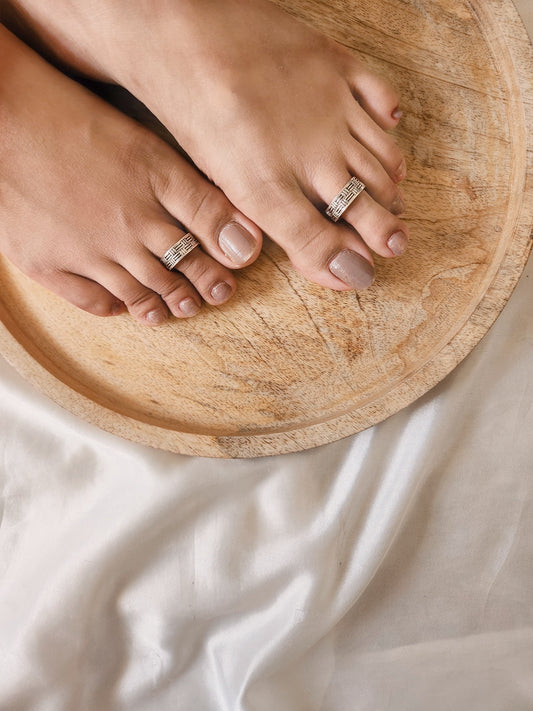 A pair of elegant silver toe rings with a polished finish, featuring delicate designs and an adjustable open band.