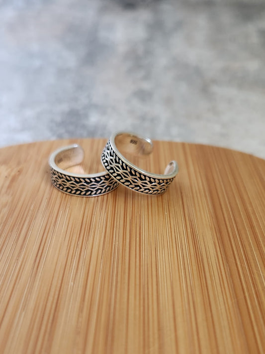 A pair of elegant silver toe rings with a polished finish, featuring delicate designs and an adjustable open band.