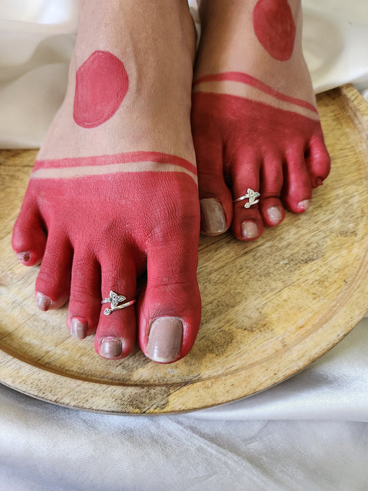 A pair of elegant silver toe rings with a polished finish, featuring delicate designs and an adjustable open band.
