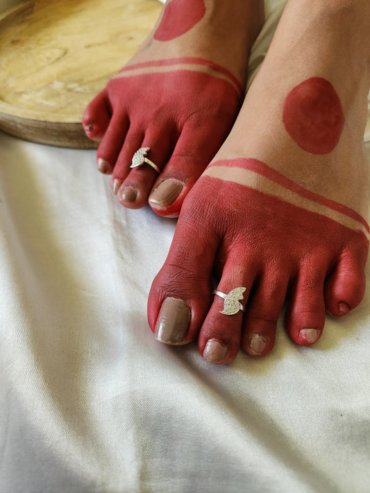 A pair of elegant silver toe rings with a polished finish, featuring delicate designs and an adjustable open band.