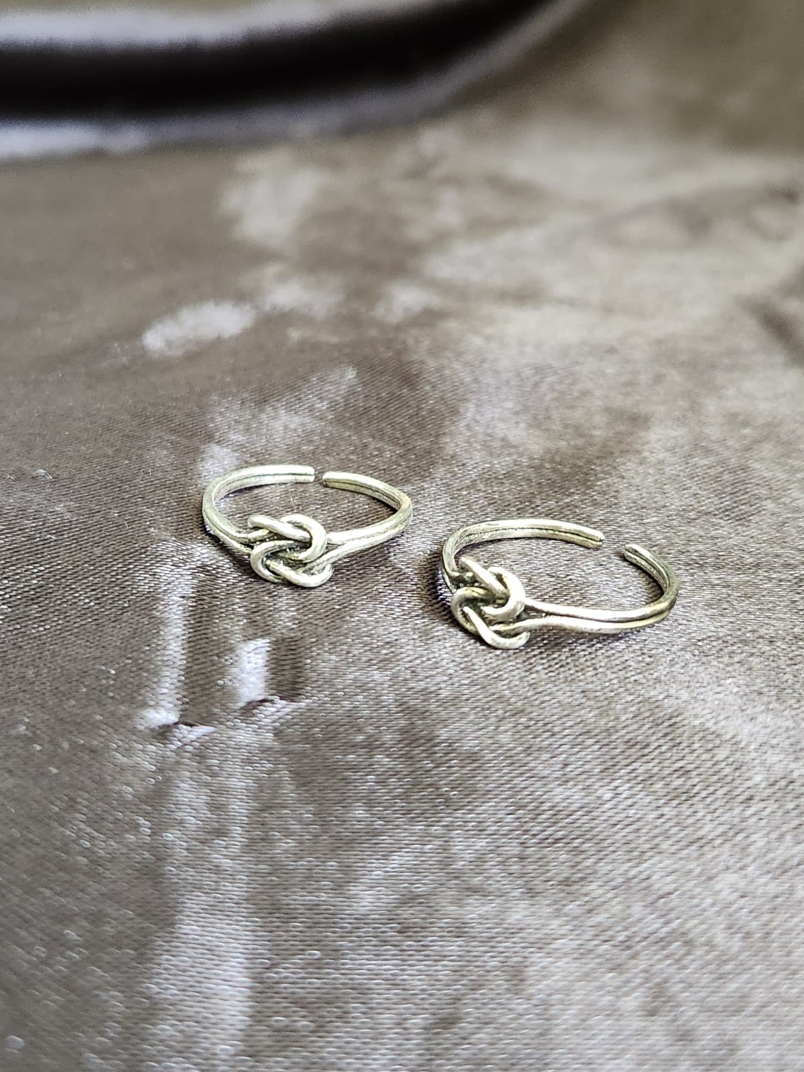 A pair of elegant silver toe rings with a polished finish, featuring delicate designs and an adjustable open band.