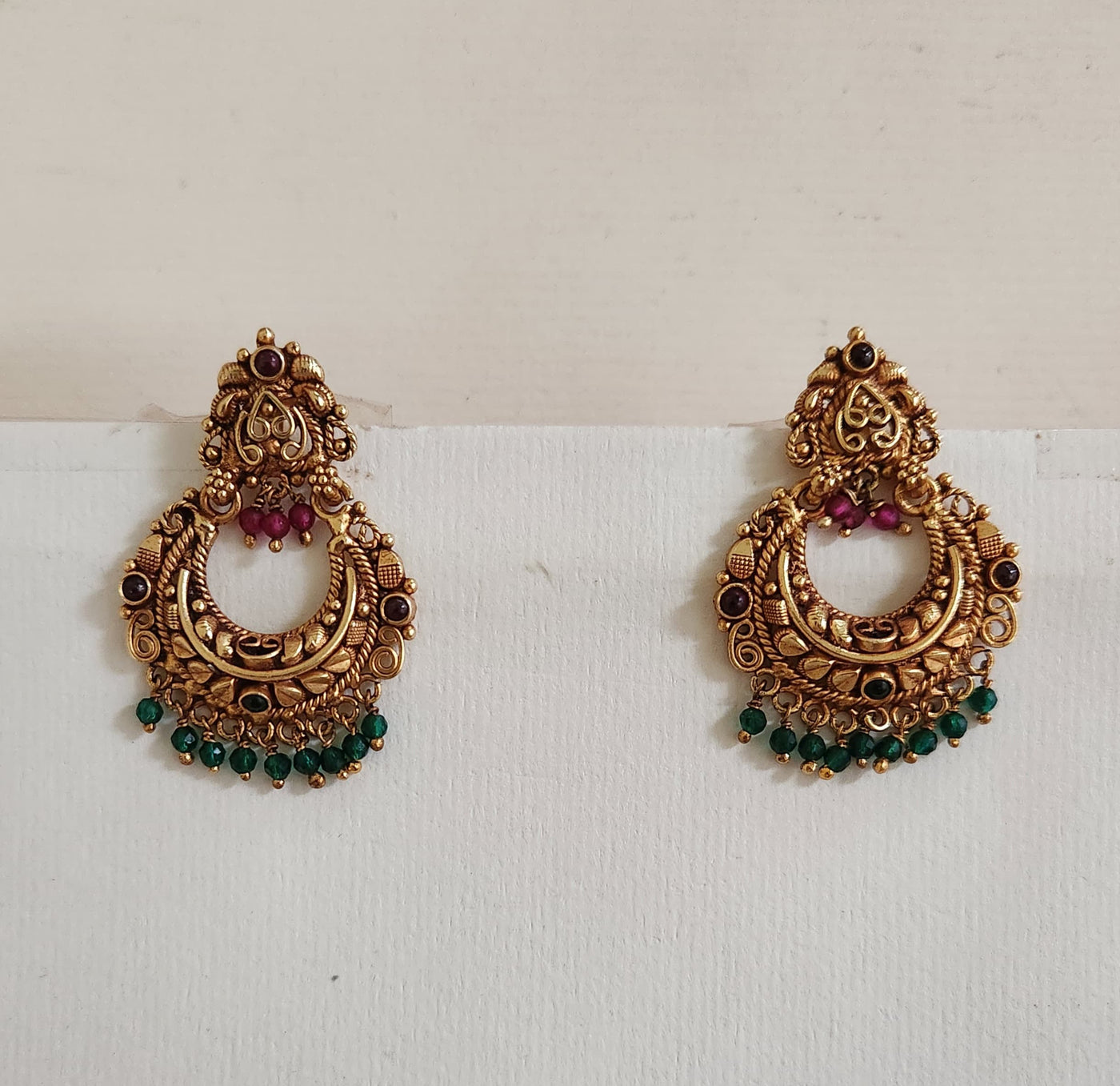 A pair of silver earrings with intricate designs, featuring red and green accents, displayed against a white background.